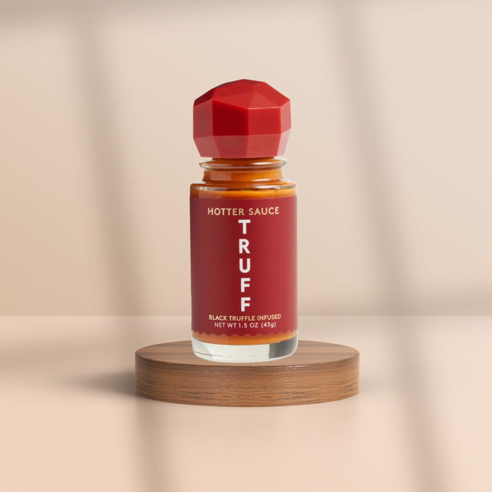 A bottle of hot sauce on a wooden stand against a neutral background.
