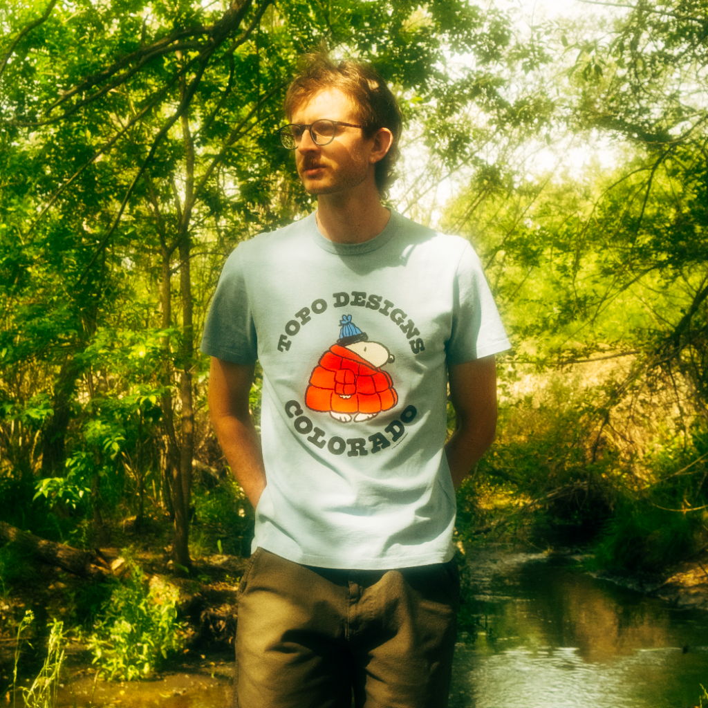 Person standing by a stream, wearing a t-shirt with a graphic design.