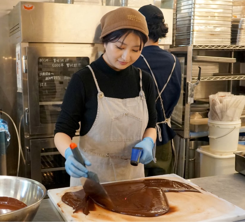 Woman preparing chocolate in a kitchen, wearing gloves and an apron.