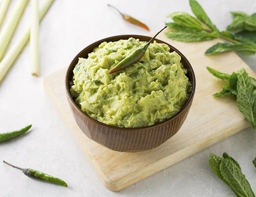 Bowl of green dip garnished with herbs, placed on a wooden board.