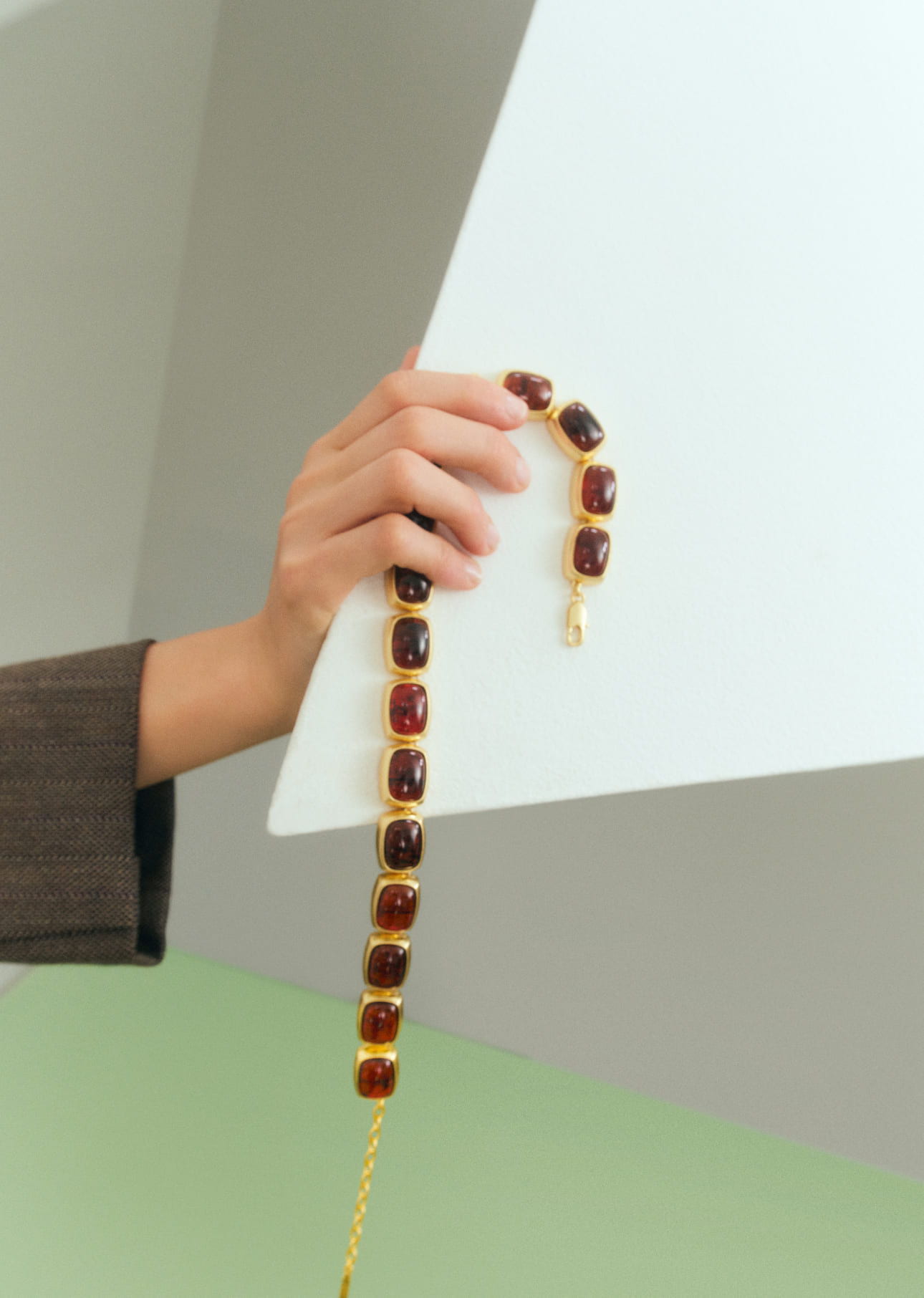 Hand holding a decorative necklace against a geometric background.