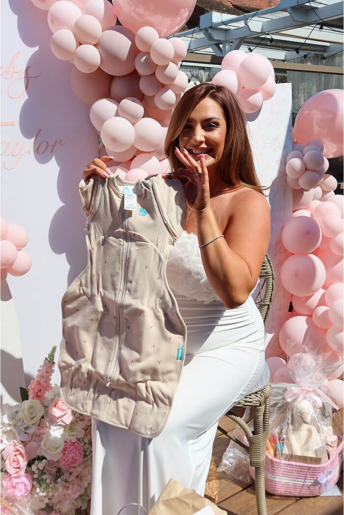 Woman in white dress holds up a beige outfit against a backdrop of balloons.