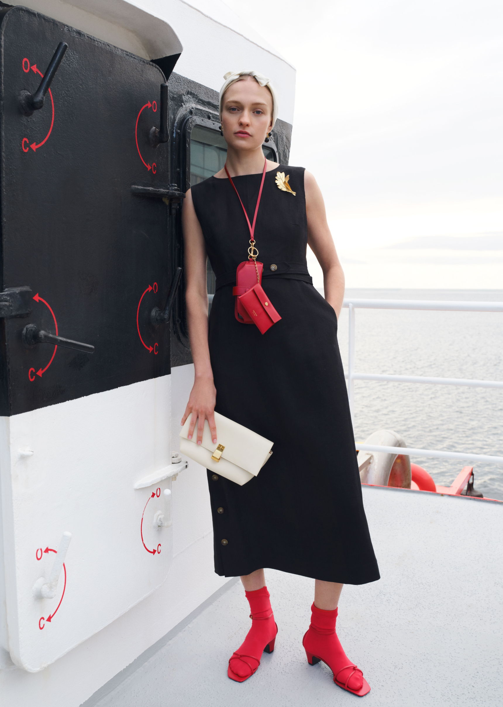 Model in black dress and red accessories on a ship deck.