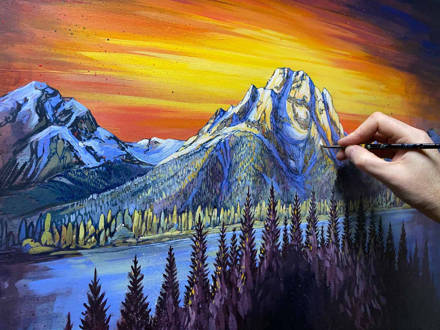 A hand painting a mountain landscape during sunset.