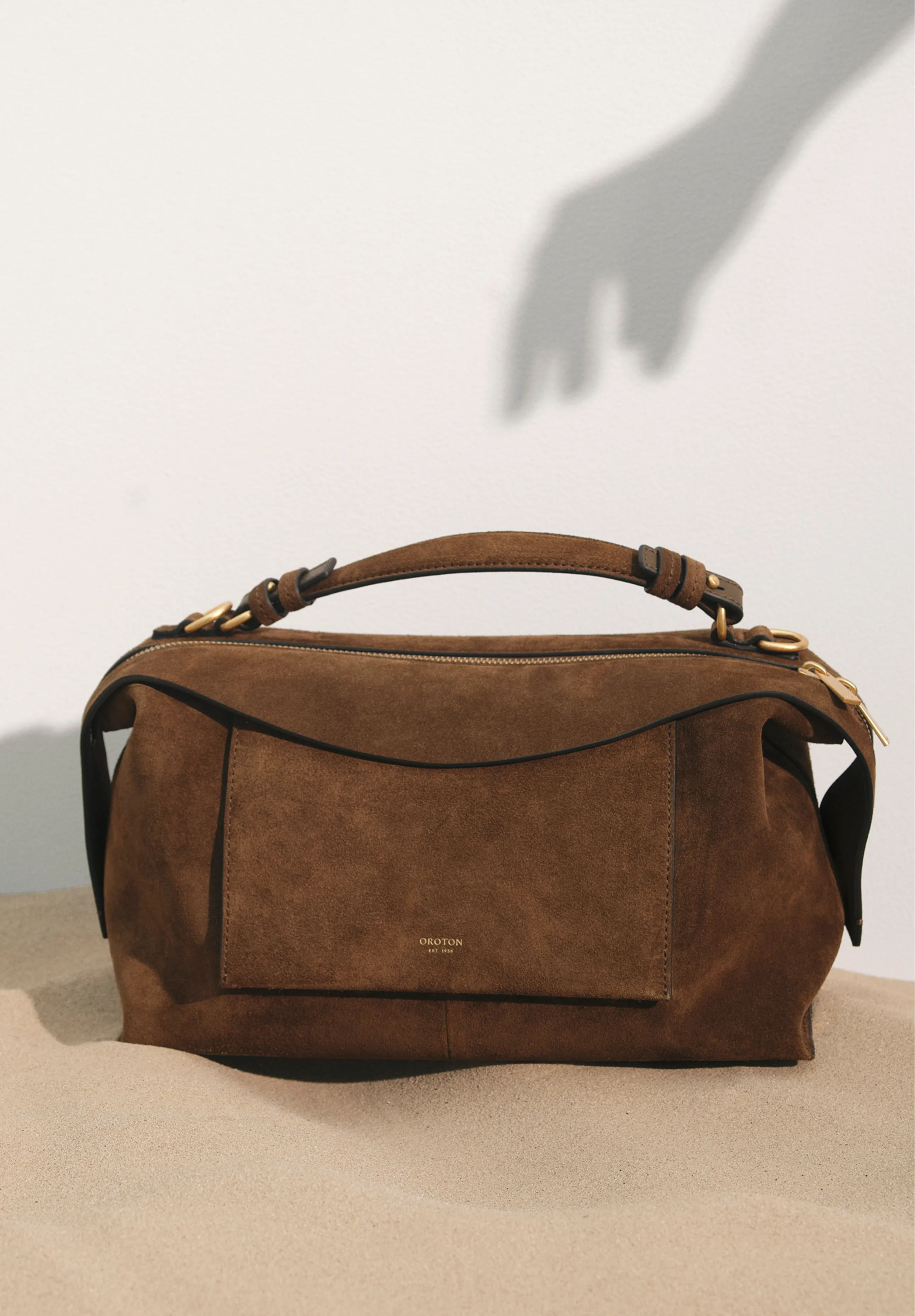 Brown suede handbag on a surface with a shadowed hand in the background.