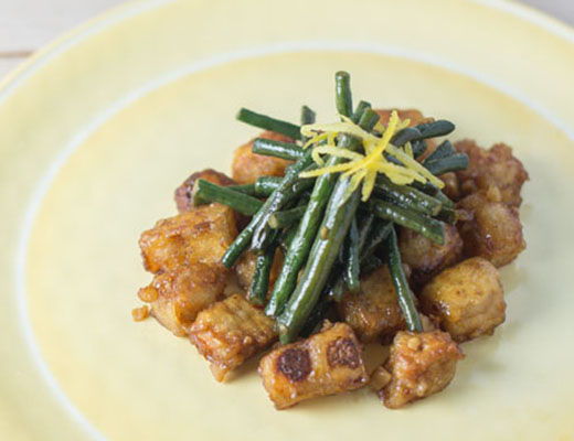 Stir-fried vegetables and tofu garnished with chives and lemon zest on a plate.