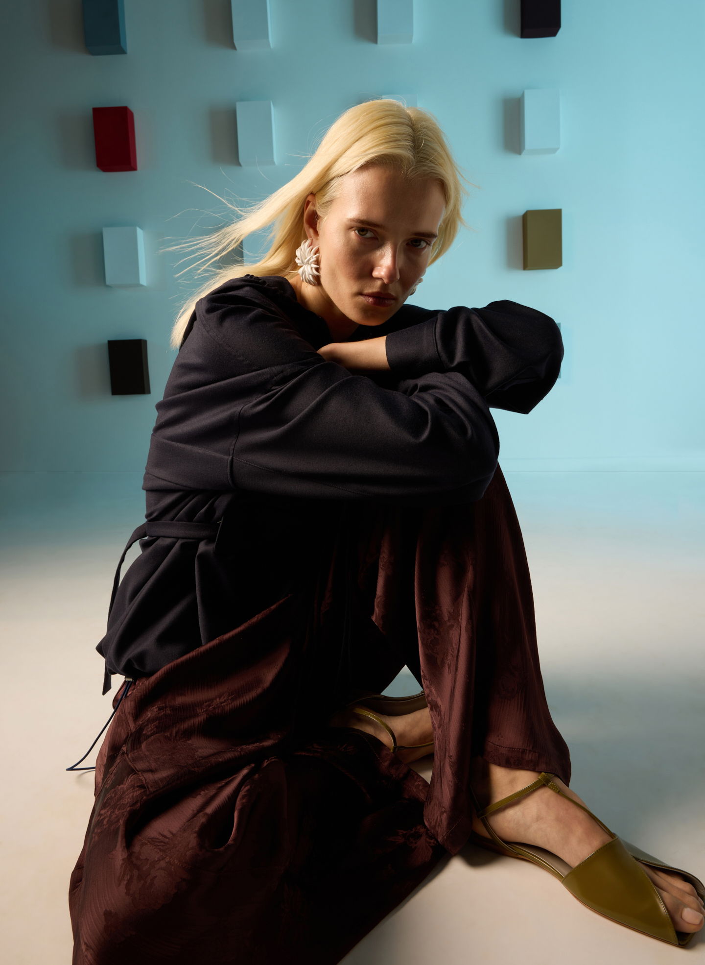 A woman sitting on the floor, wearing stylish clothes, against a colorful background.