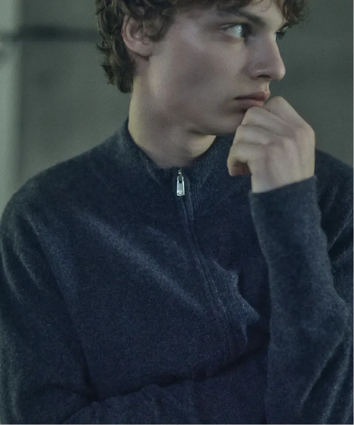 A young man in a zip-up sweater looking thoughtfully to the side.