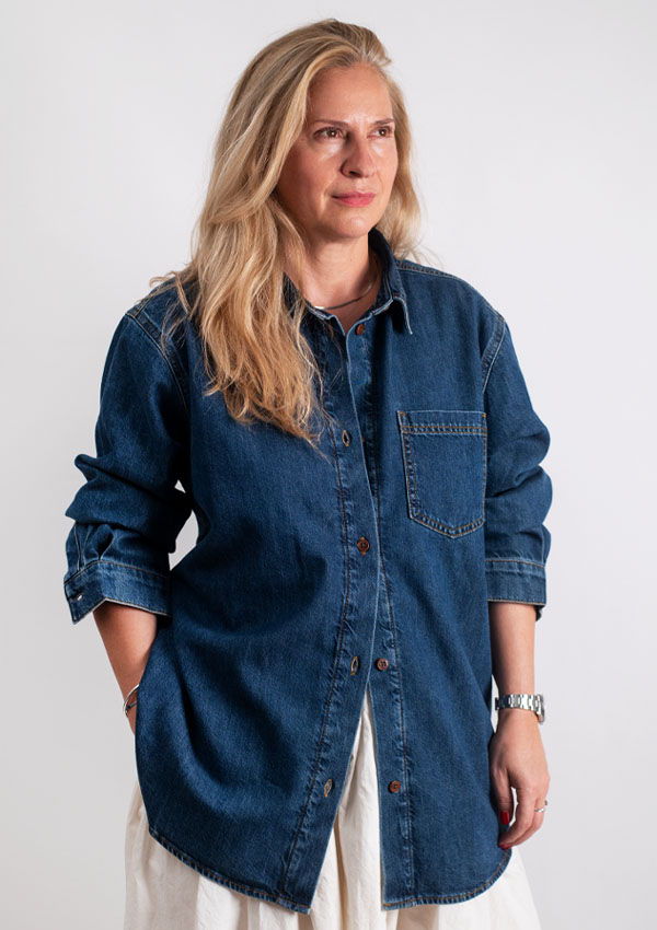 Kat wearing a denim shirt, standing against a light background.
