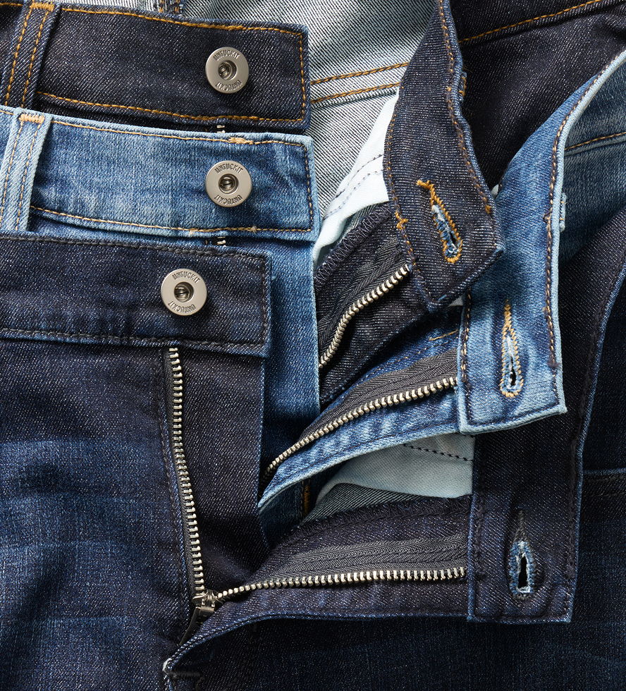 Various pairs of jeans folded, showcasing buttons and zippers.