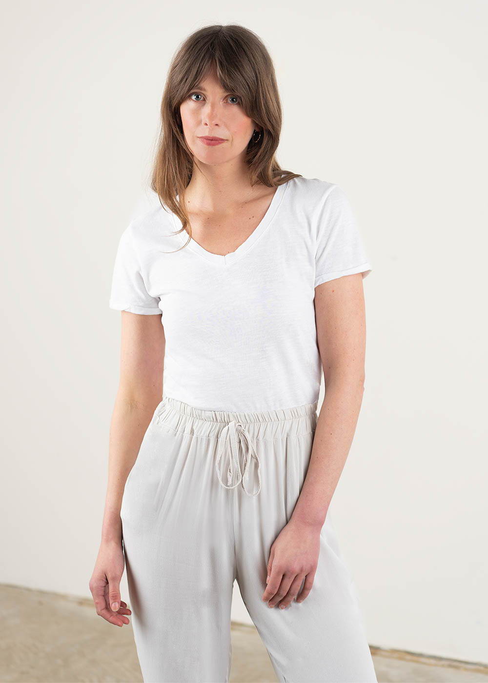 A model wearing a white, v neck short sleeved t shirt