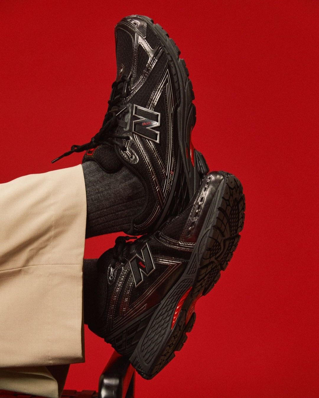 A close-up of black New Balance shoes against a red background.
