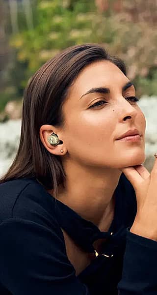 A woman with earbuds, thoughtfully resting her chin on her hand.