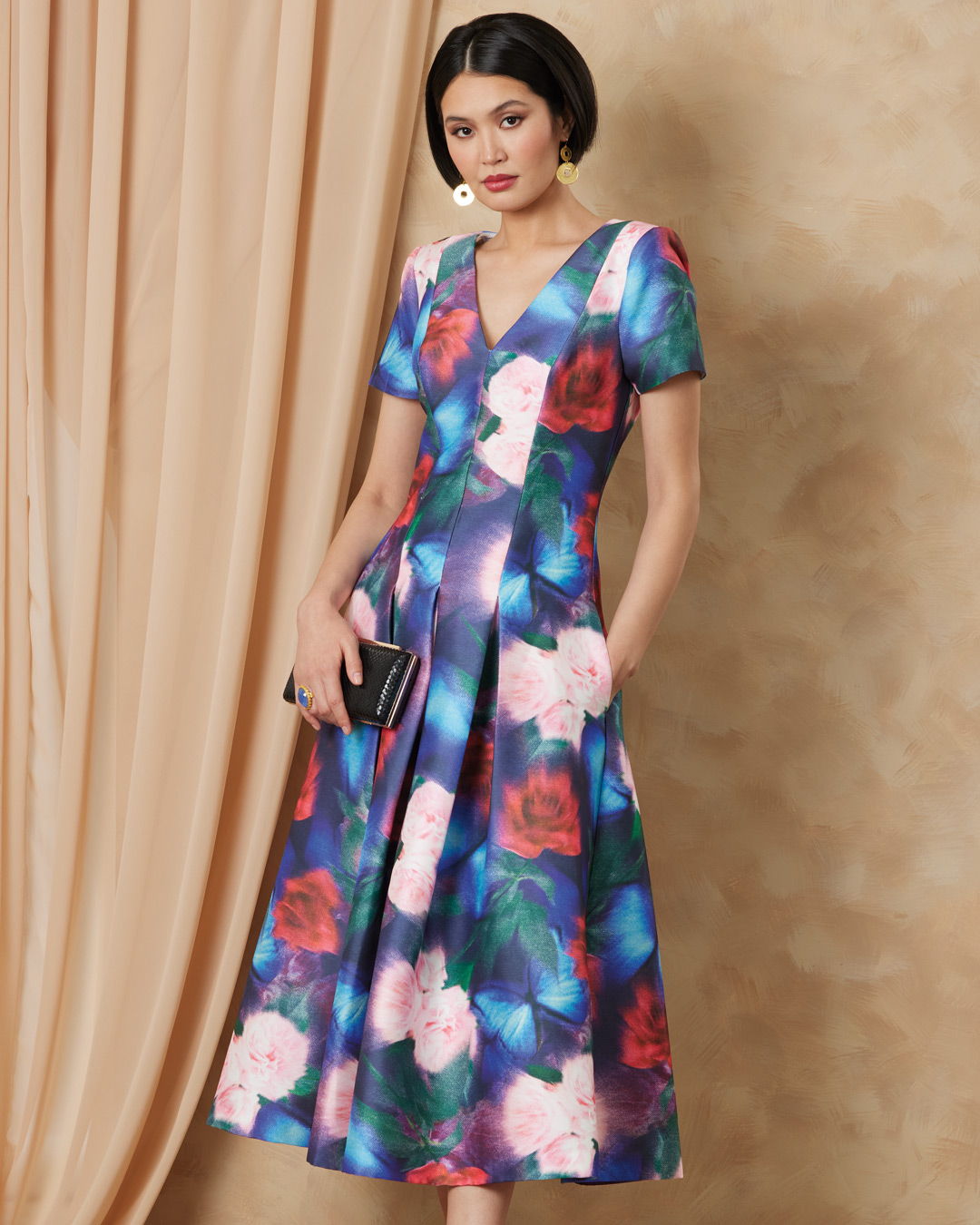 Woman wearing a colorful floral dress with a v-neck and pockets.