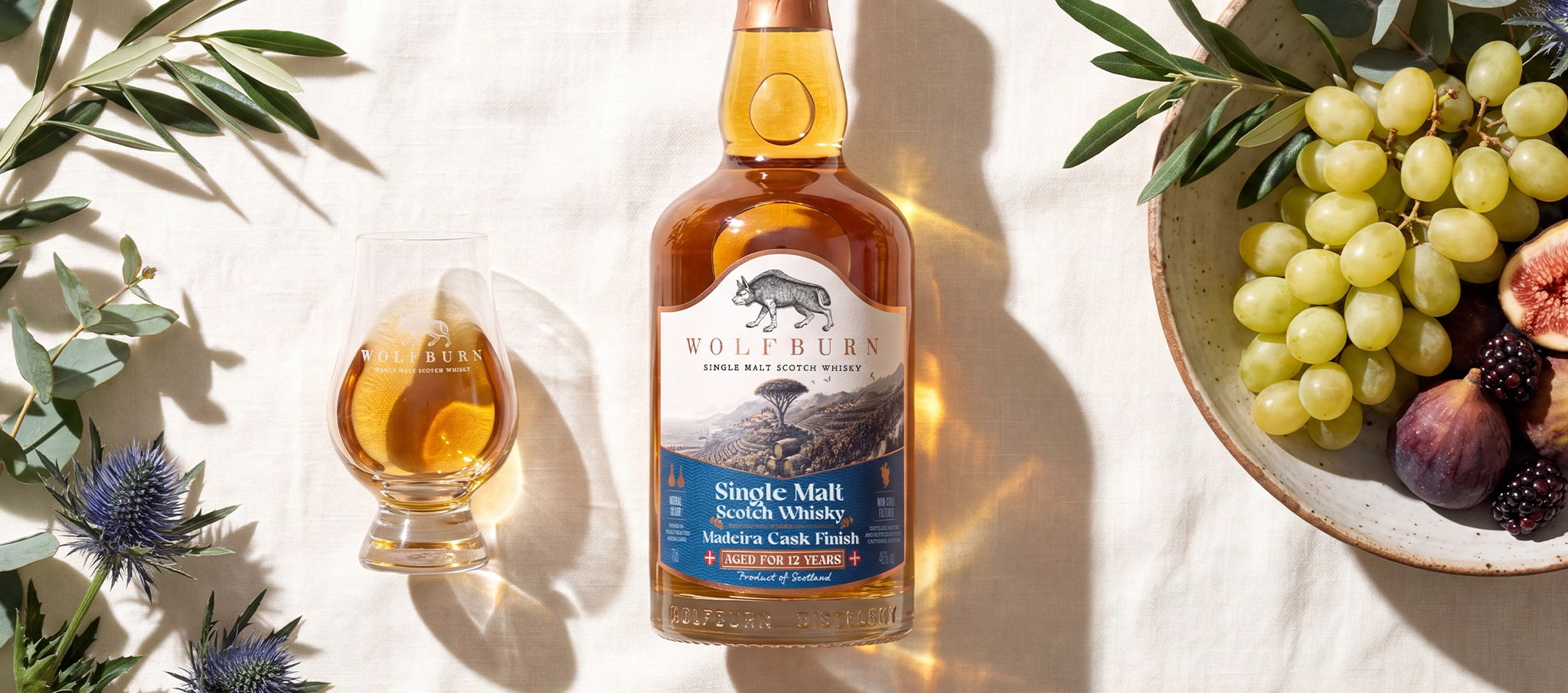 Madeira cask finish bottle on sun drenched background with fruit and glass of whiskyy