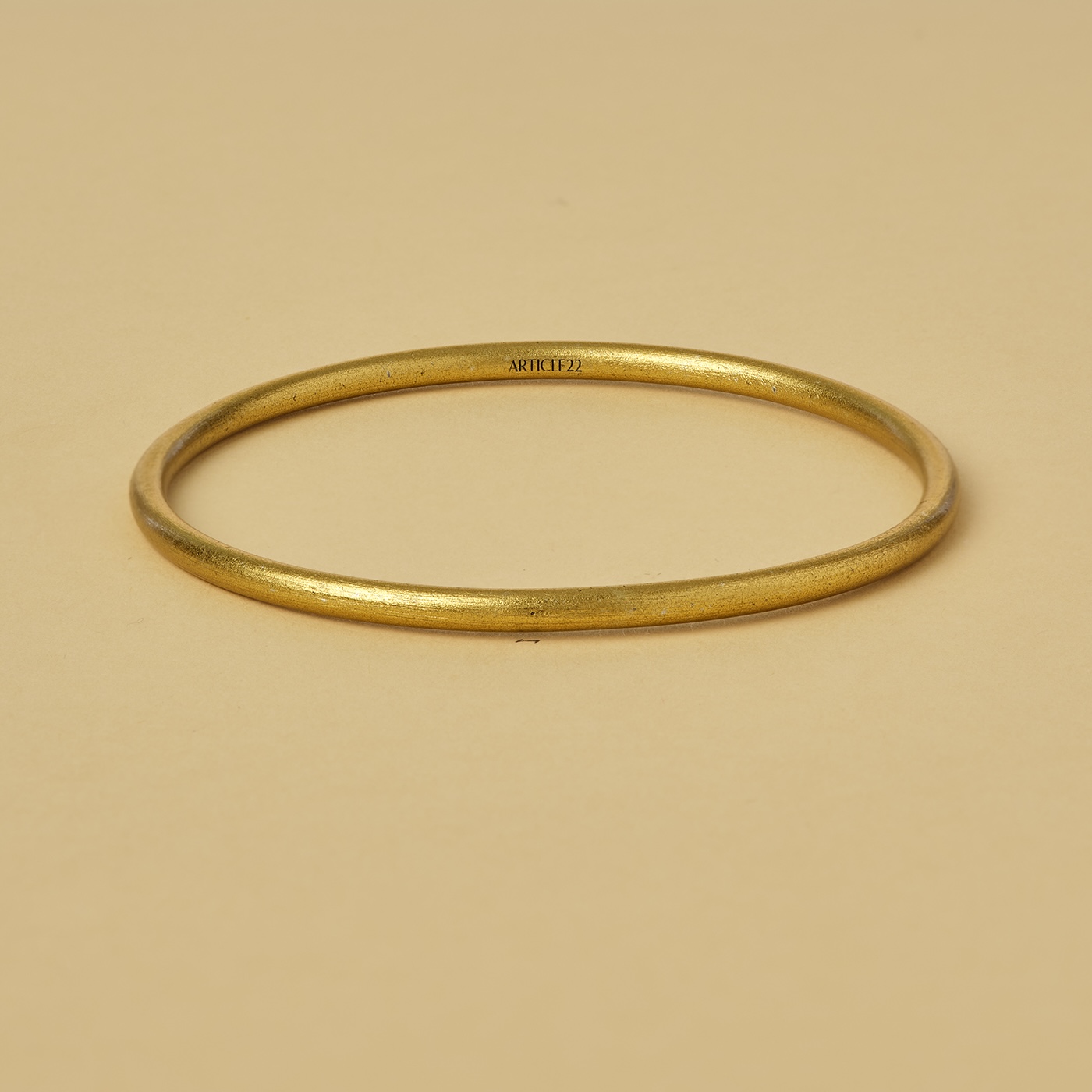 A gold bangle bracelet on a card with a circular brushstrokes symbolizing virtue.