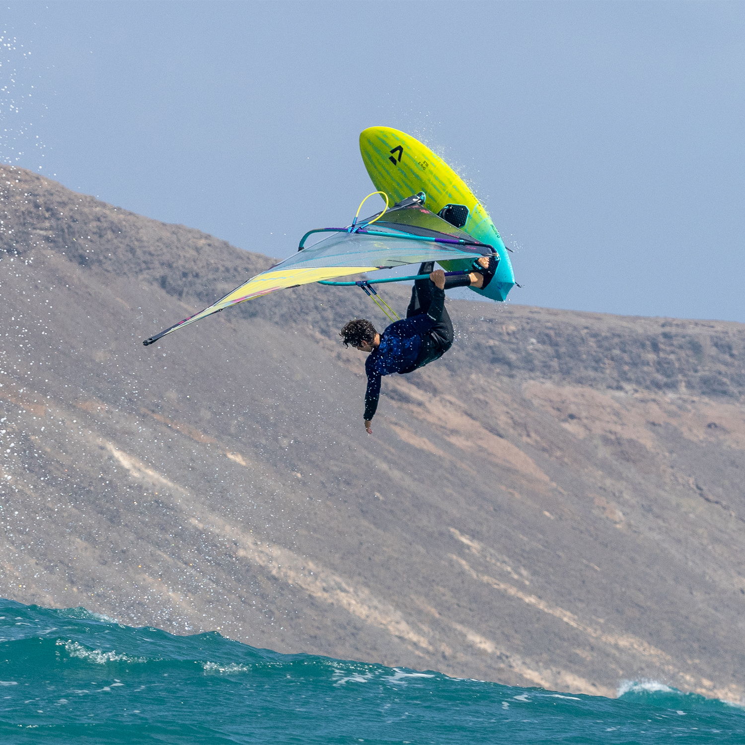 Une personne faisant de la planche à voile en plein vol au-dessus des vagues de l'océan, avec les montagnes en arrière-plan.