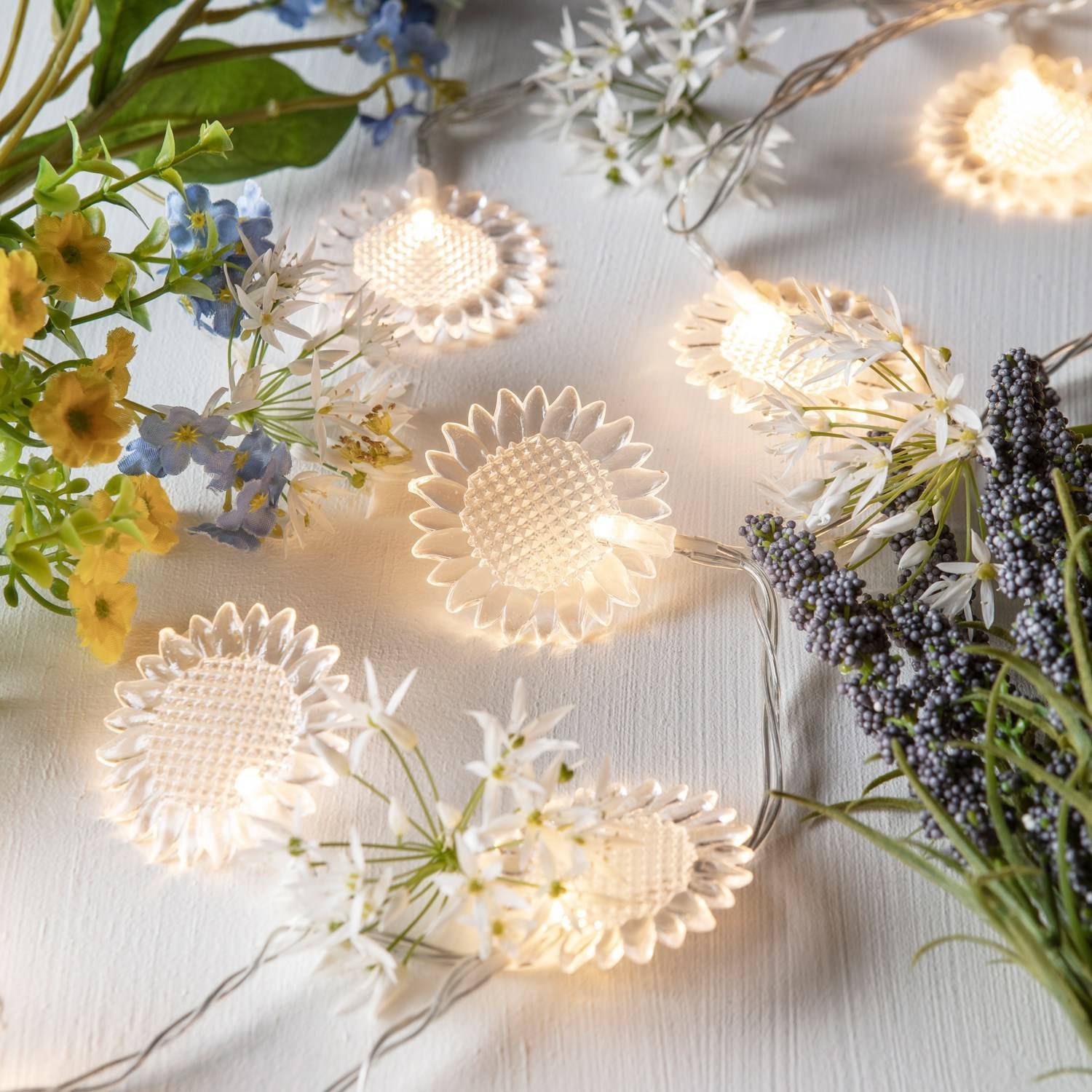 Sunflower fairy lights on a white table with real flowers surrounding.