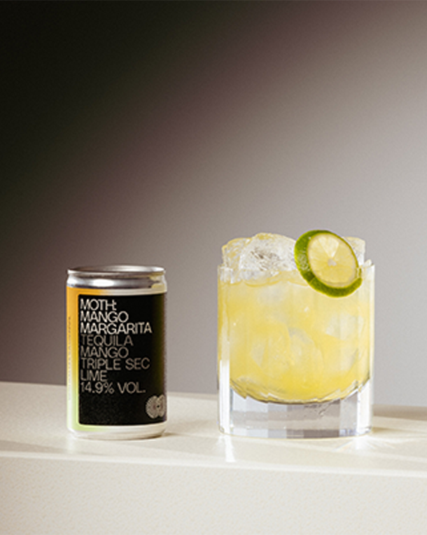 Can of margarita mix next to a glass of margarita with lime slice.