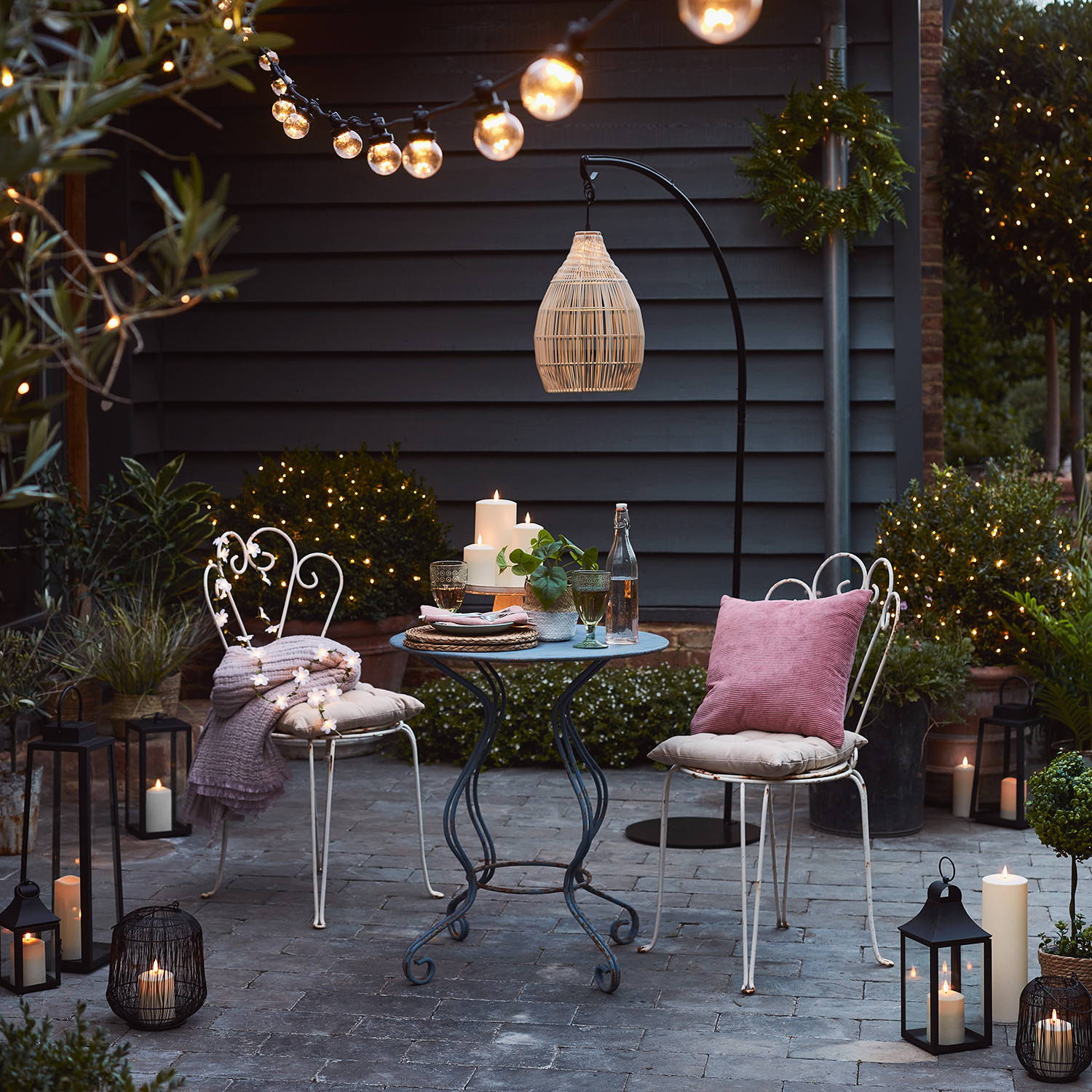 An alfresco patio setting with lanterns, LED candles, a solar pendant light and warm white festoon lights.