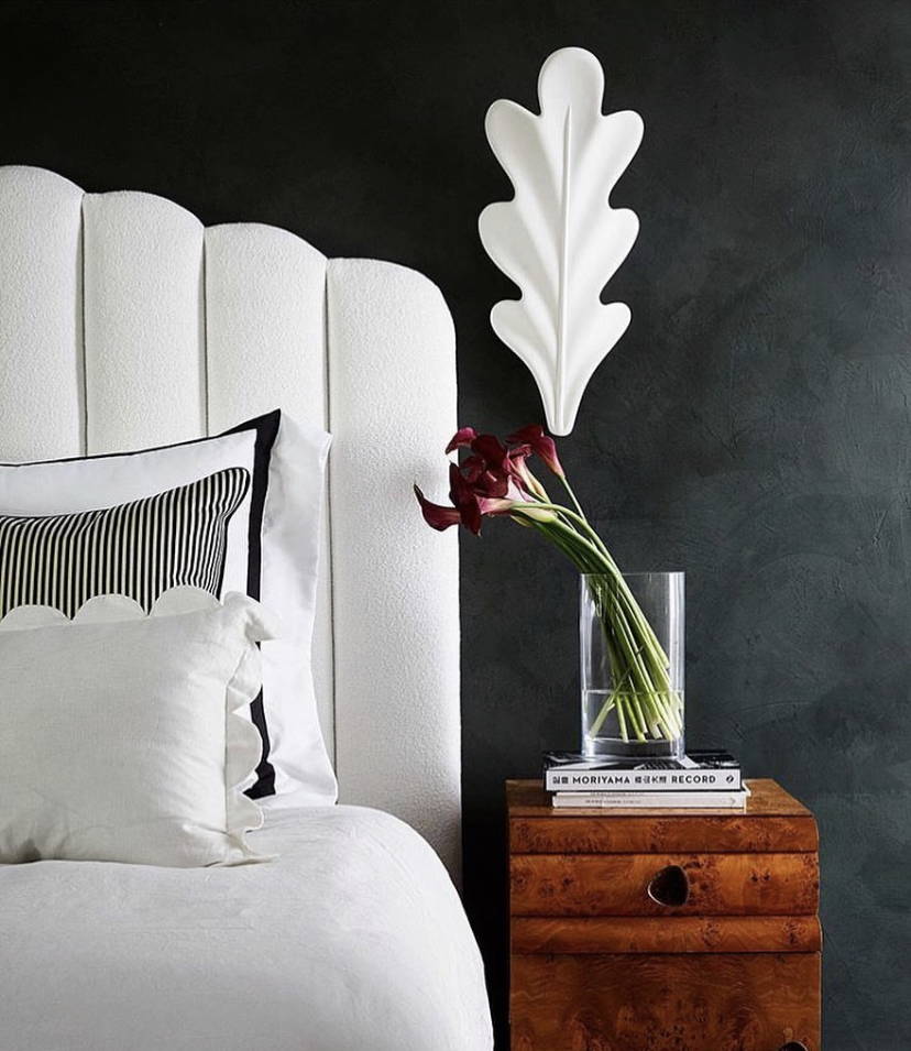 White upholstered headboard with white scallop pillow against dark grey textured wall.