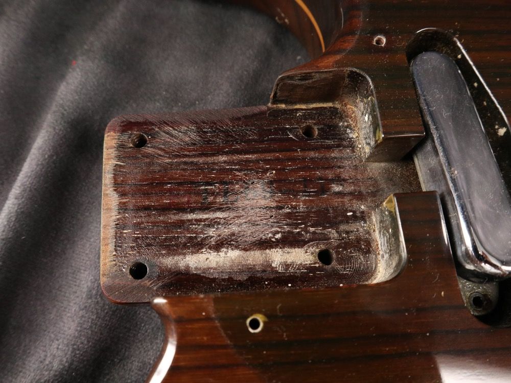 Close-up of a wooden guitar neck joint with visible wear and tear.