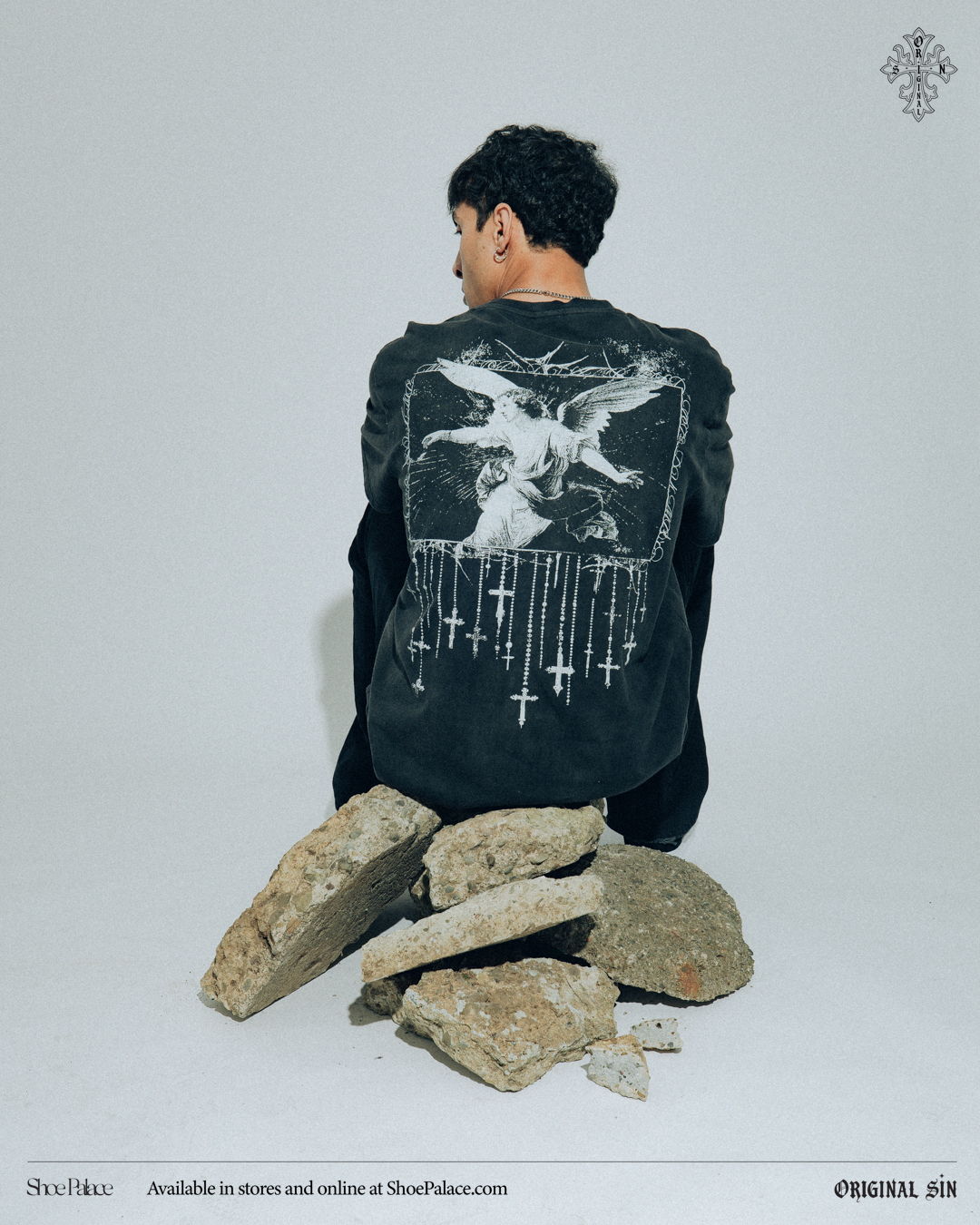 Person sitting on rocks, wearing a black shirt with graphic design on back.
