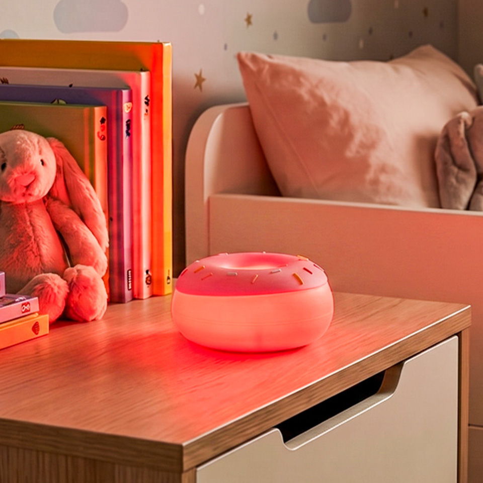 A cozy bedside table with a pink donut-shaped lamp and stuffed bunny.