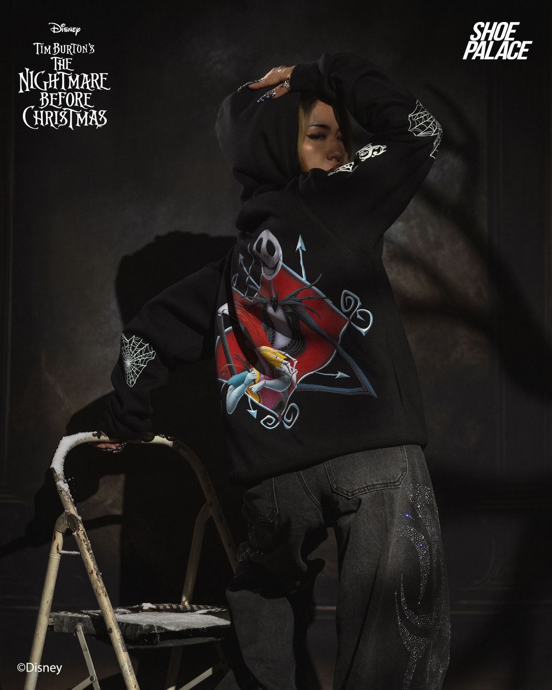 Person wearing a black hoodie with a graphic design, posing against a dark background.