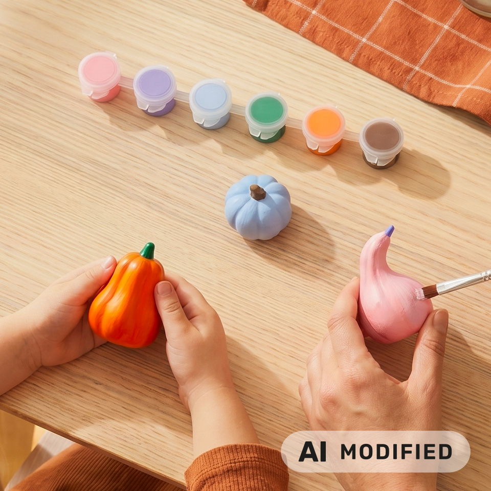 Deux mains tiennent des citrouilles peintes avec des peintures colorées sur une table en bois.