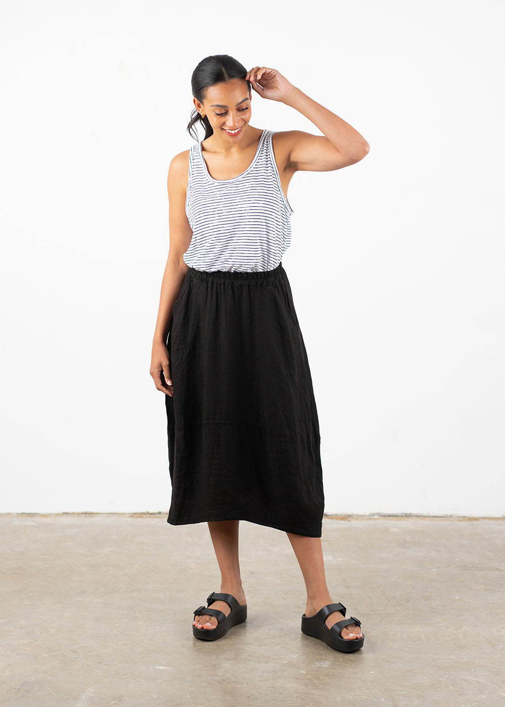 A model wearing a black and white sleeveless top with a black linen tulip shaped skirt with black chunky platform slides