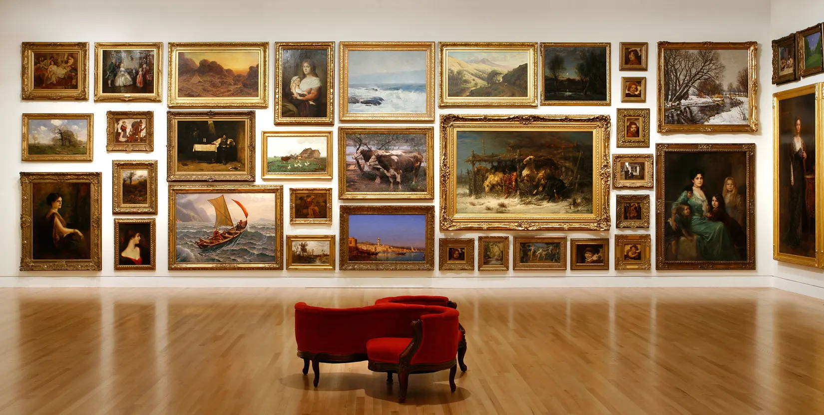 museum room with a collage of paintings along the walls., and  a red couch in the middle of the room
