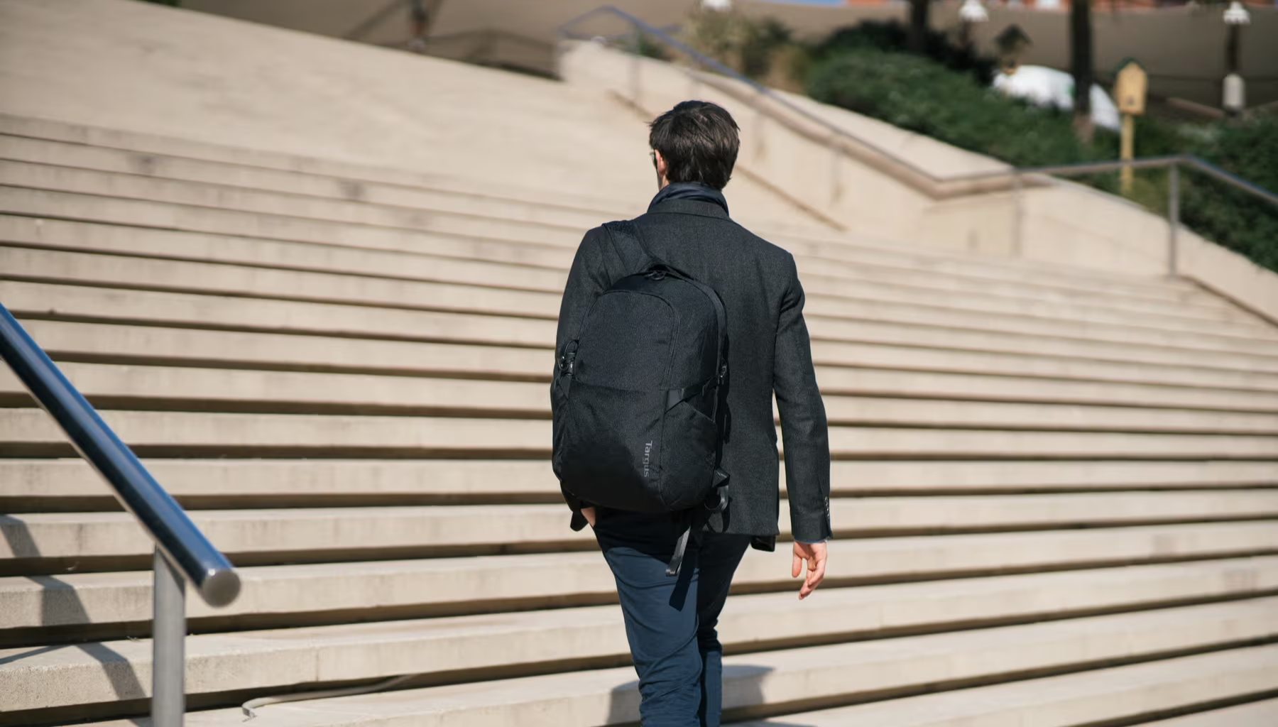 an in a business suit walking up outdoor steps wearing a black Targus backpack.