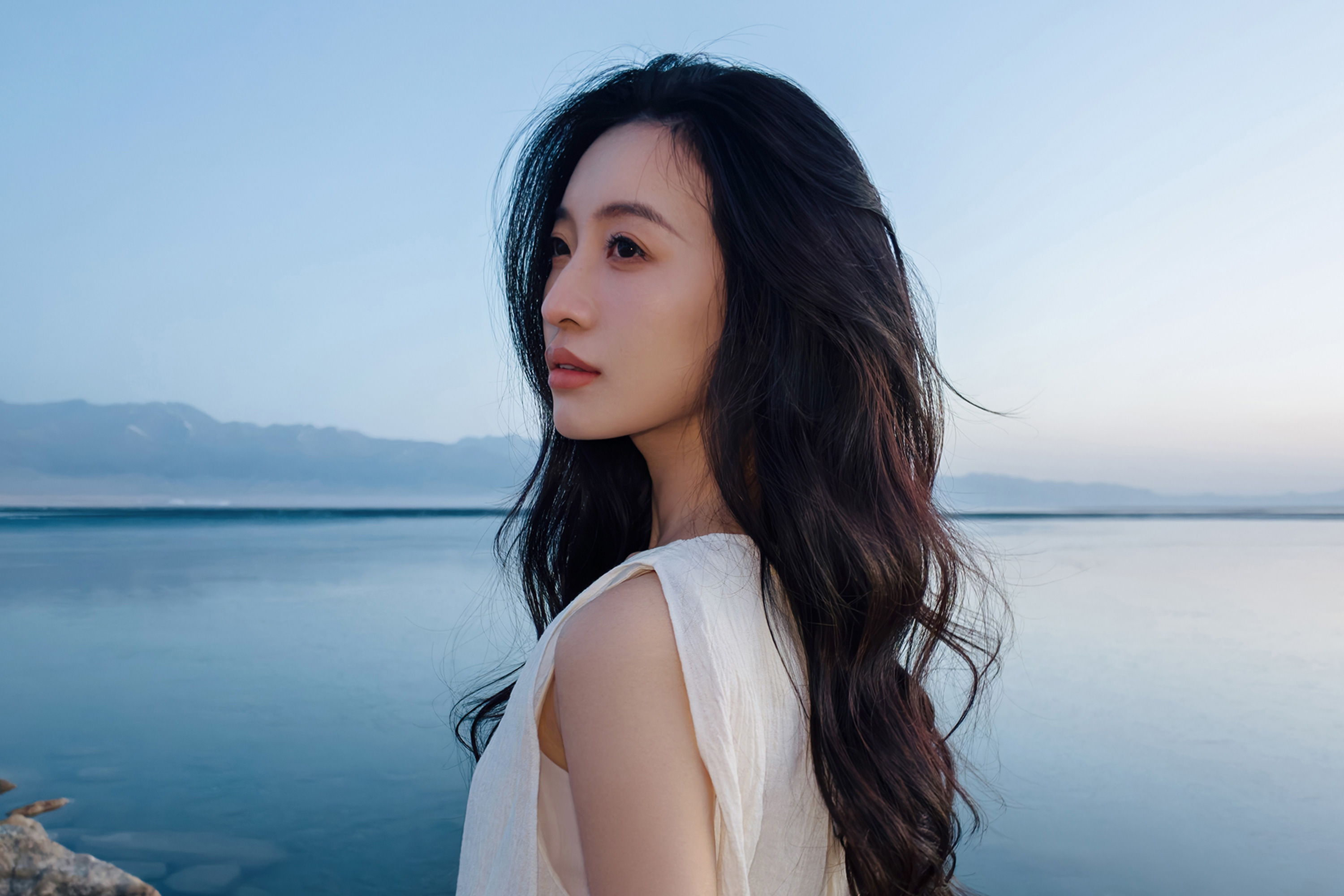 Woman with long hair gazing at the water during sunset.