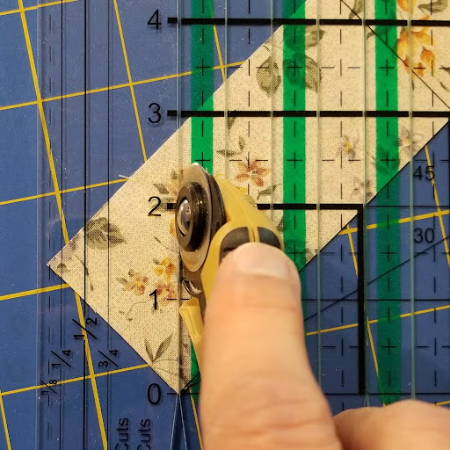 Cutting a triangular fabric piece for a quilt block with a rotary cutter and shape cut ruler