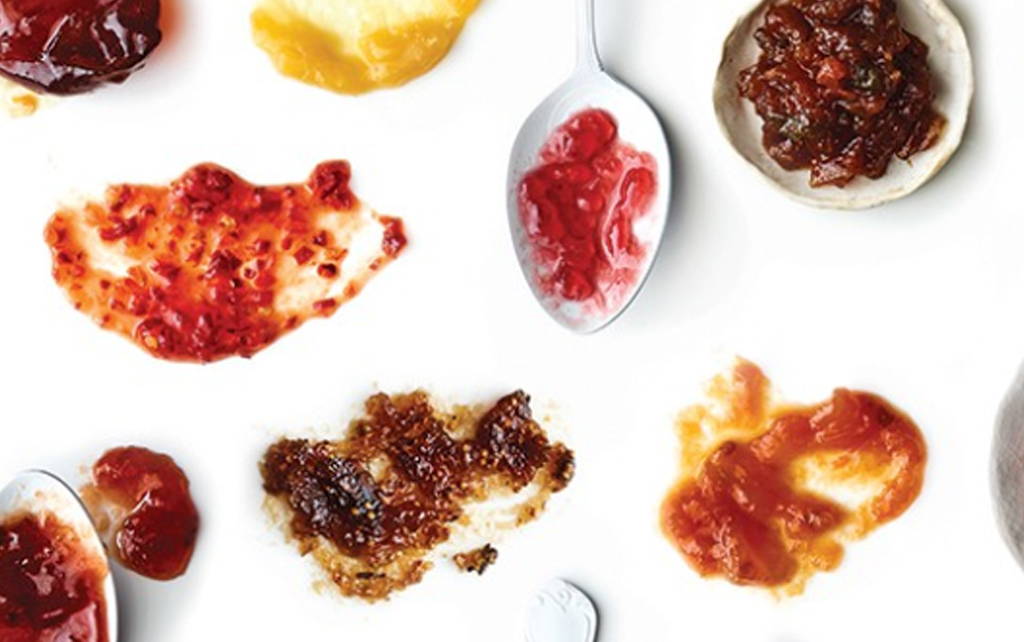 Small amounts of jam are artistically smeared on a white counter top. One spoon has jam on it. 