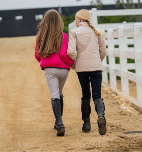 Equestrian bestfriends hanging out at the barn one is wearing a bright pink jacket and the other a tan puffer jacket. Shop outerwear now!