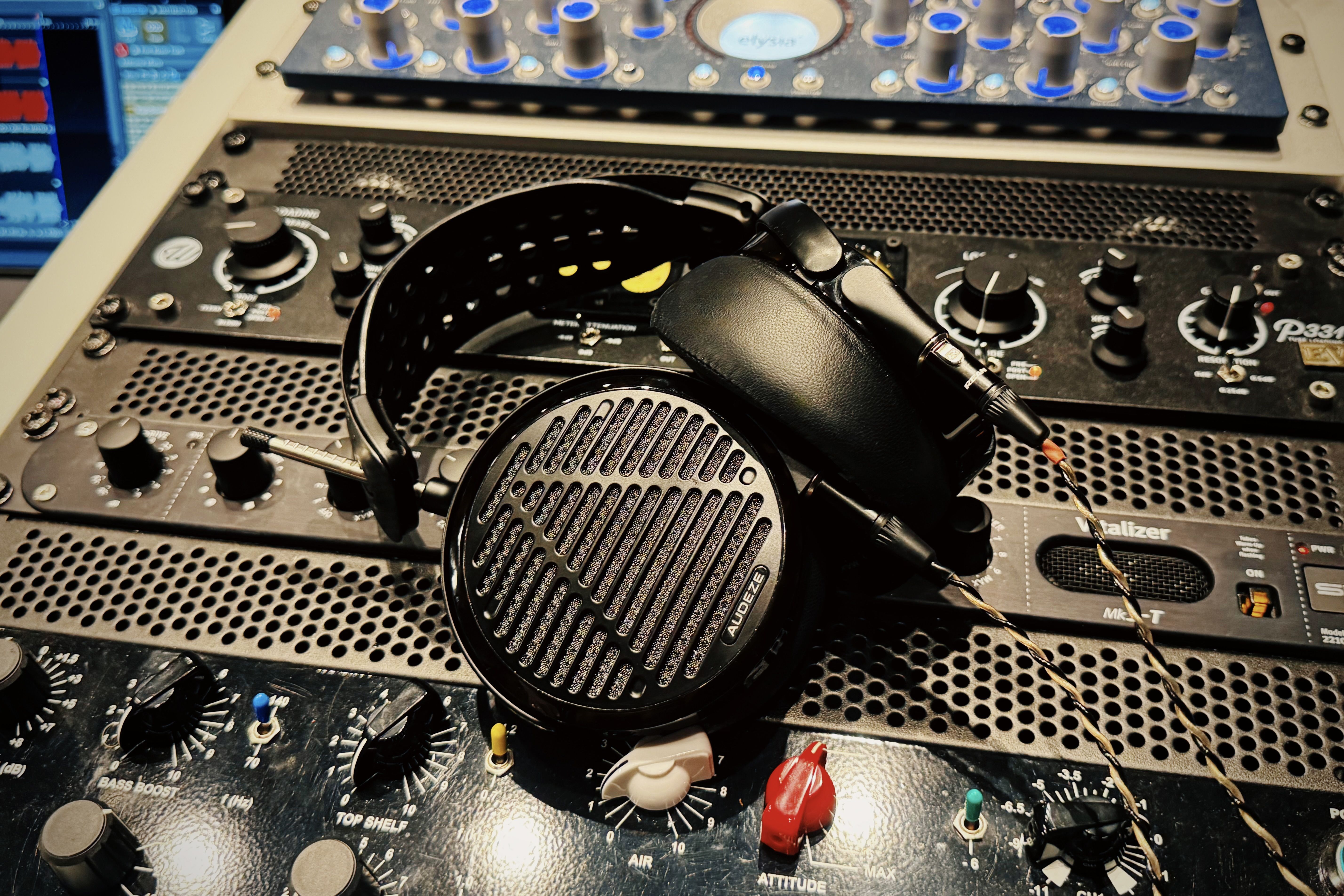 Audeze LCD-5 headphones resting on audio equipment with knobs and controls.