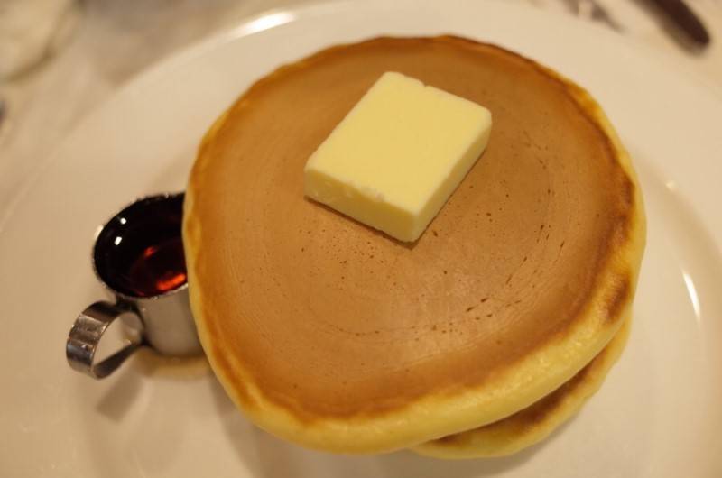 A picture of 2 layers of pancake served with butter and syrup