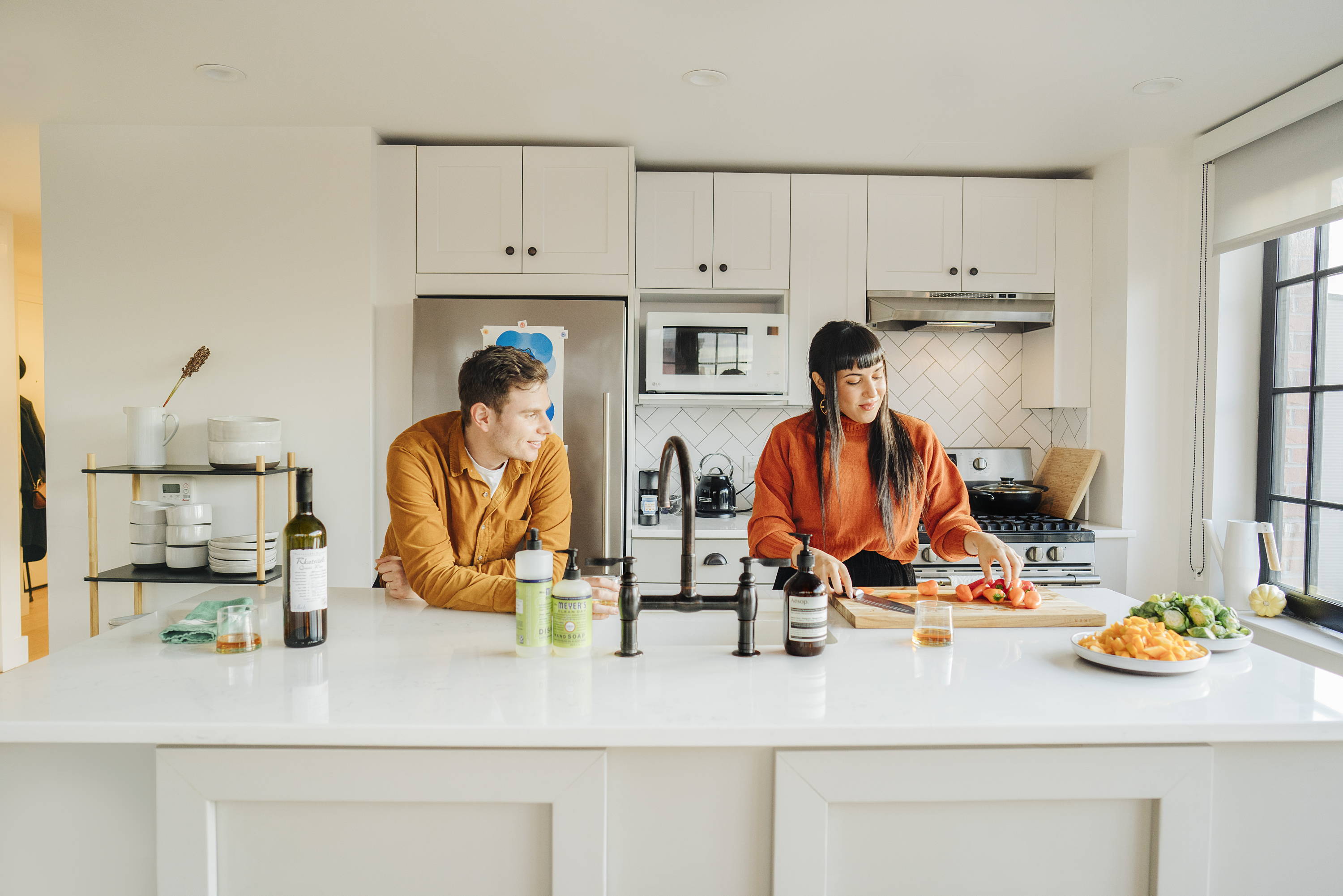 Two people cooking in light and airy but small kitchen with white shelves and tile