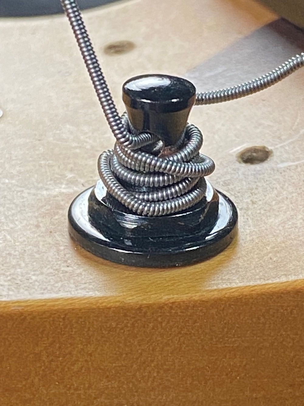 Schwarzer Knopf mit gewickeltem Draht auf einer Holzoberfläche.
