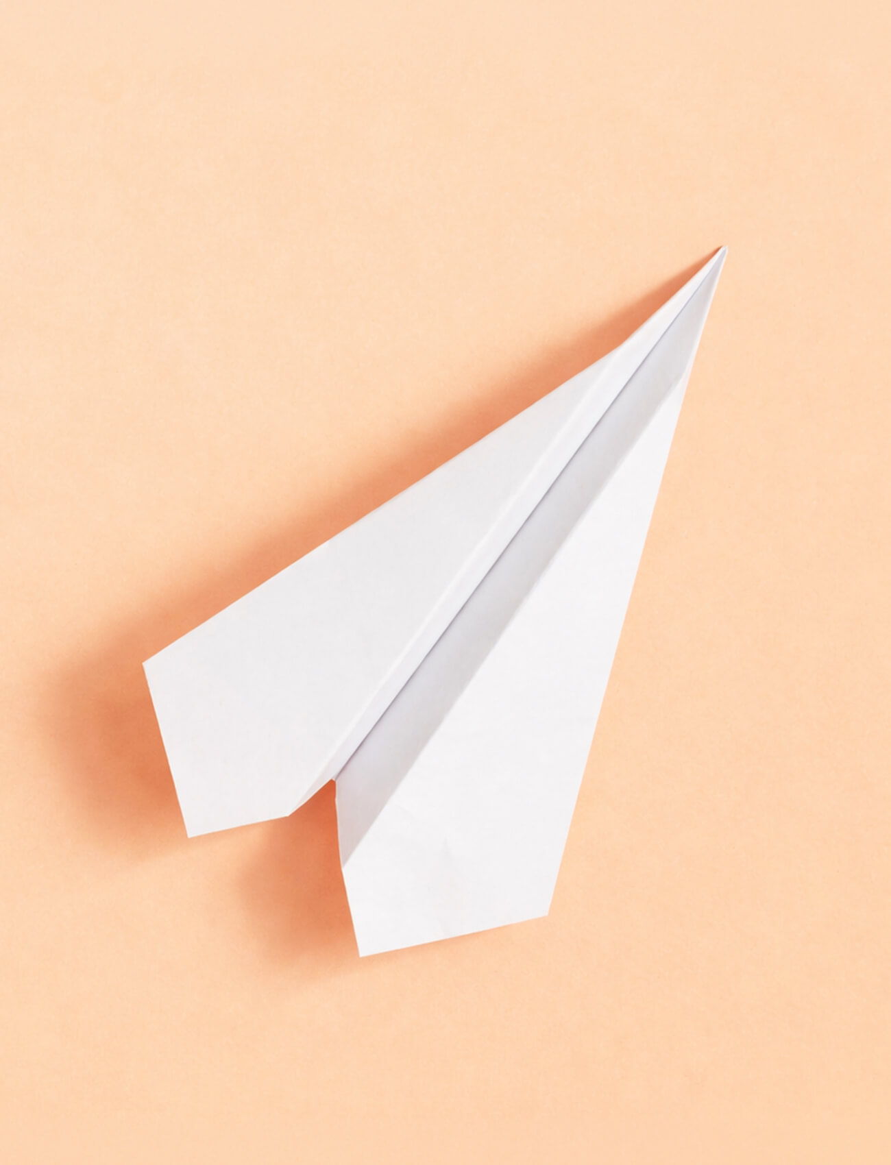 A folded white paper airplane on a peach background.