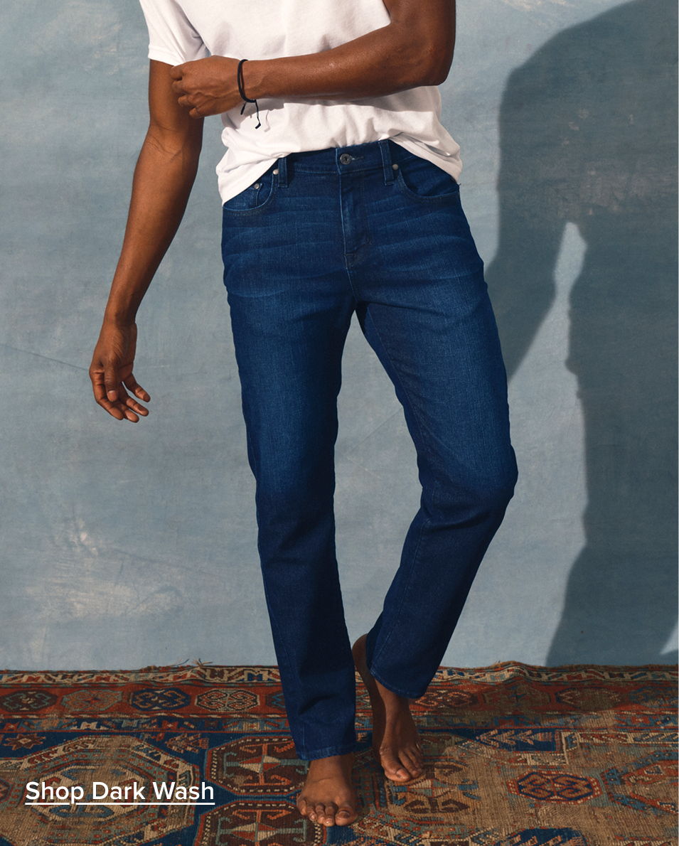 Person wearing dark wash jeans and a white t-shirt, standing on a carpet.