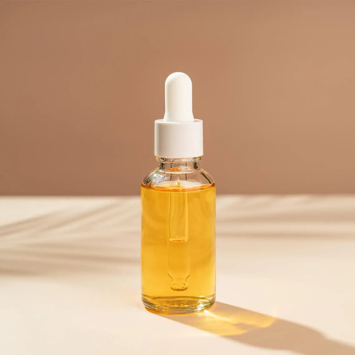 A glass dropper bottle filled with yellow oil on a light surface.