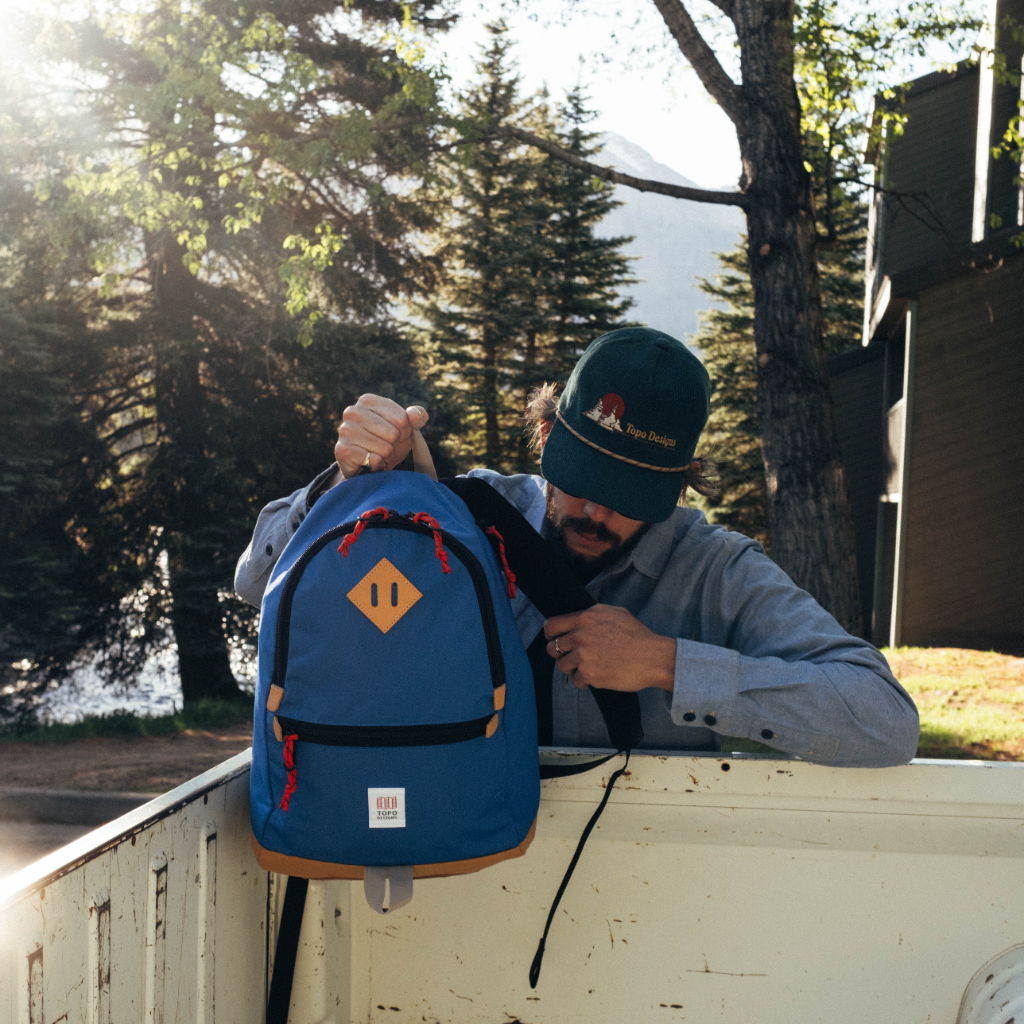 Person with a blue backpack adjusting it in a sunlit outdoor setting.