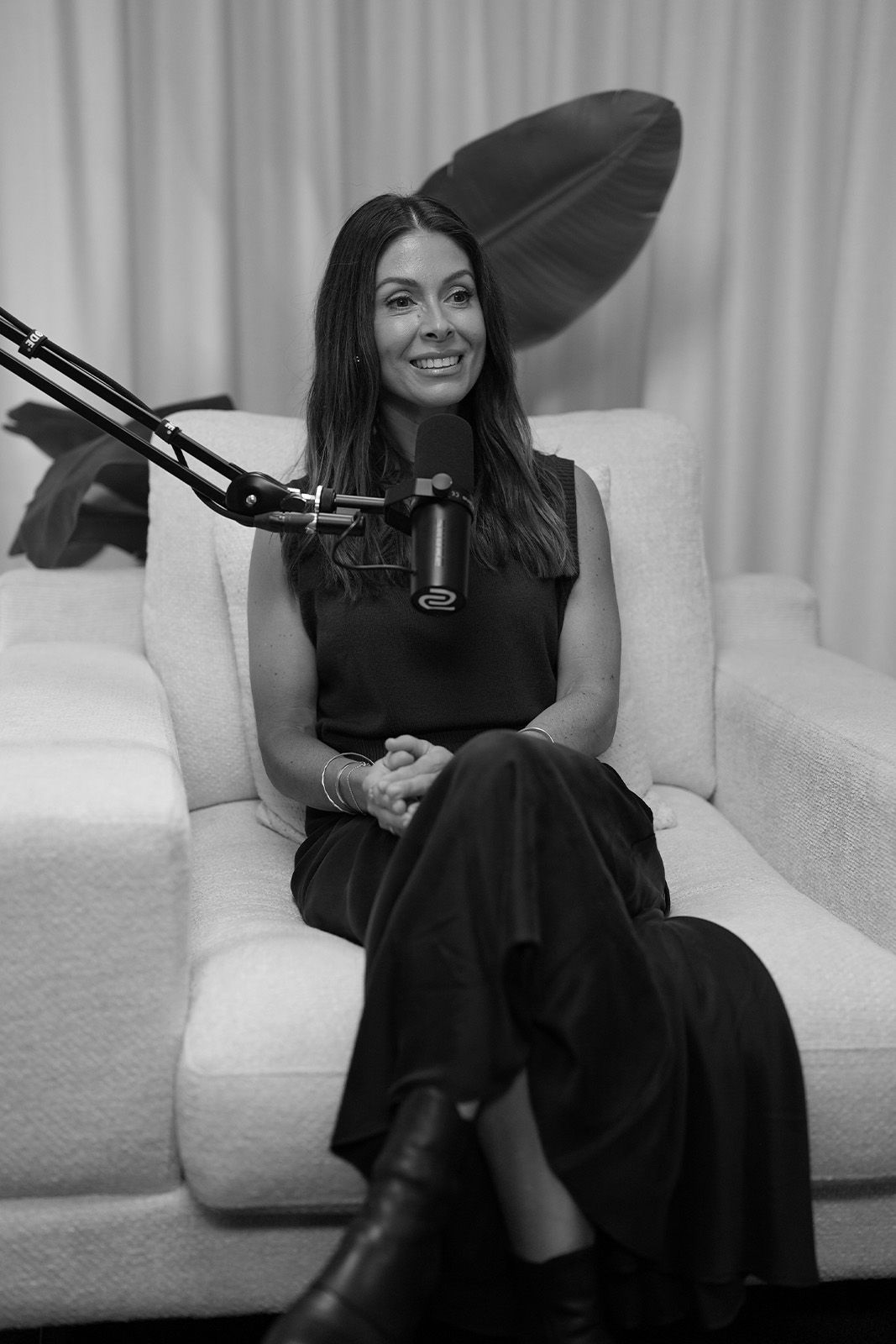 Woman sitting on a couch with a microphone, smiling in black and white.