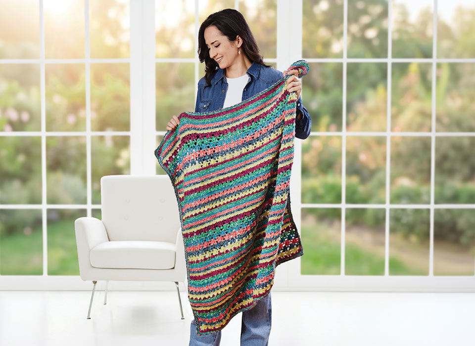 Woman holding a colorful blanket in a bright, airy room.
