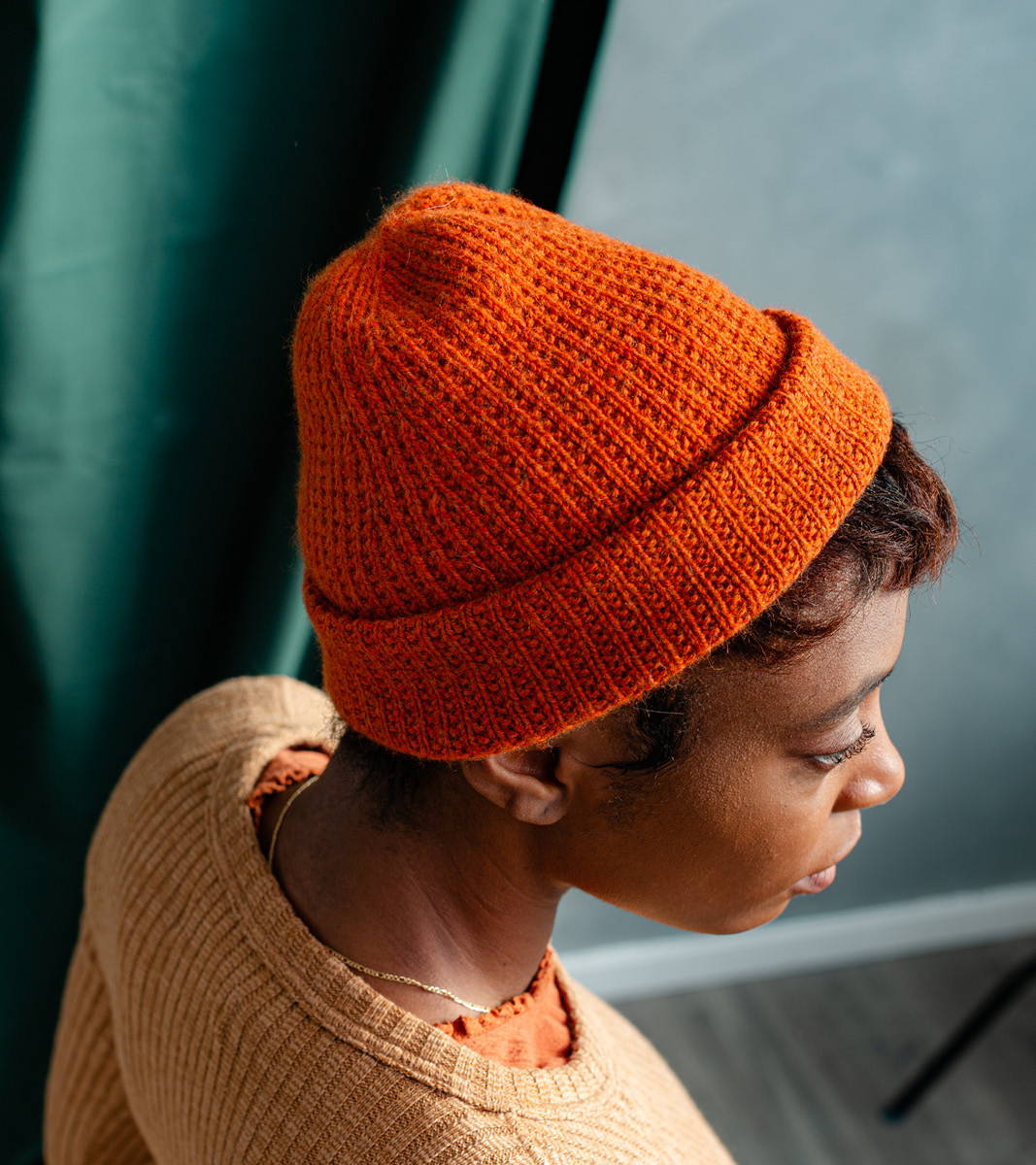 Maya, a woman with short brown hair, models Brooklyn Tweed's Stroopwafel Hat hand knit in Imbue Sport yarn color Lantern