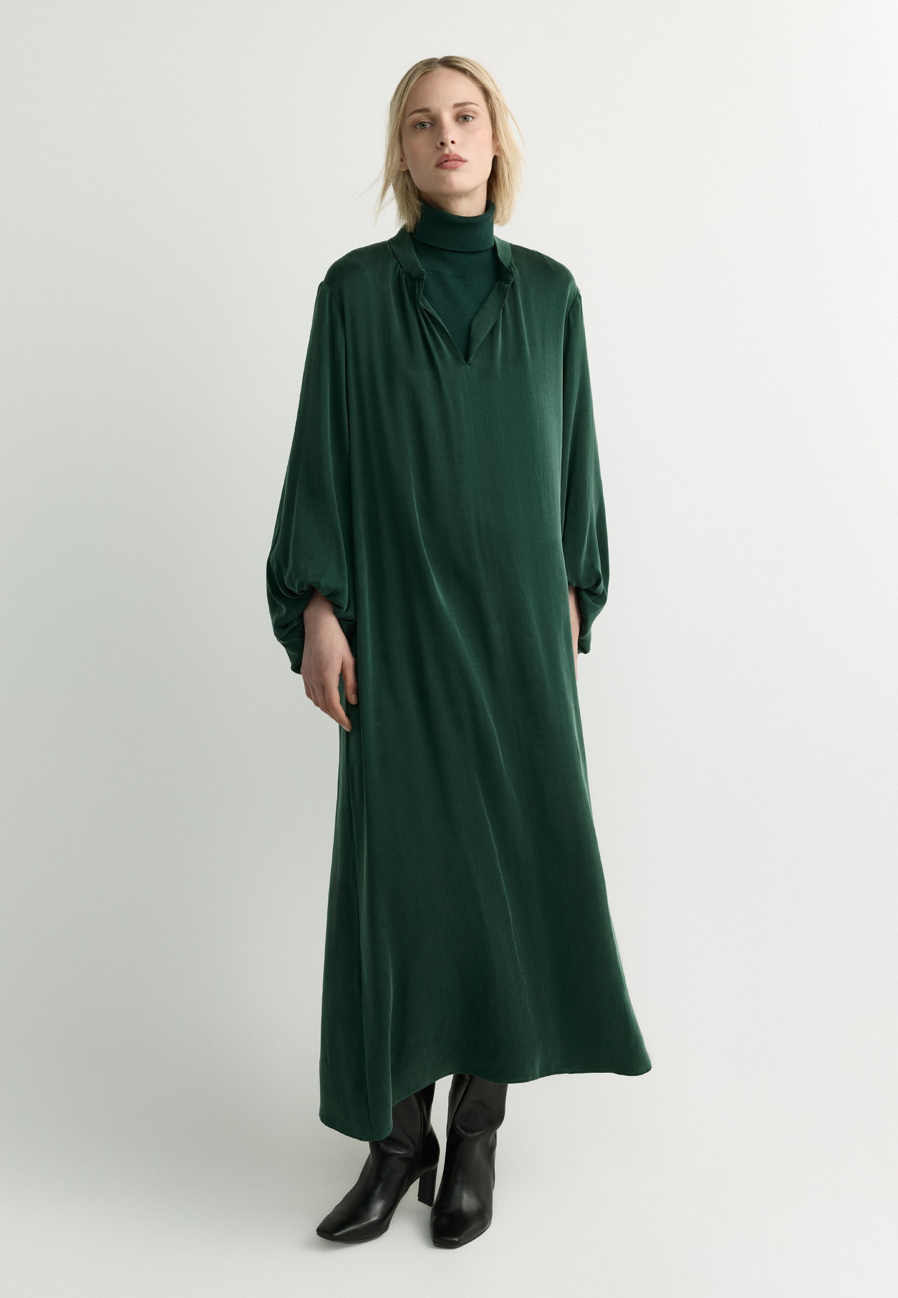 Model wearing a long green dress with puffed sleeves and black boots.