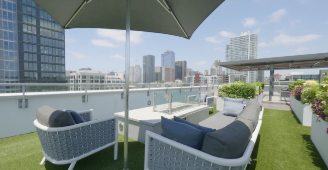 Rooftop lounge area with seating, greenery, and city skyline in the background.